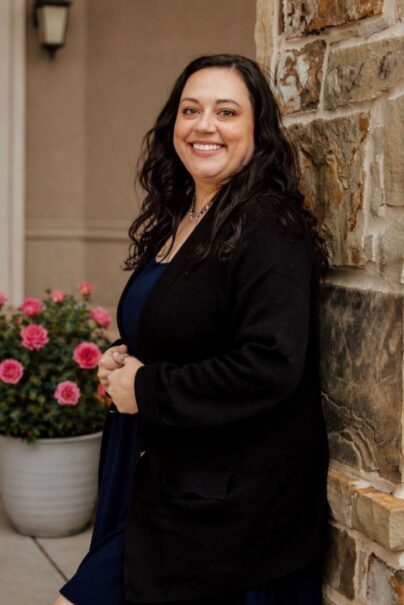 Charlotte Dortch in a black cardigan near pink potted flowers.